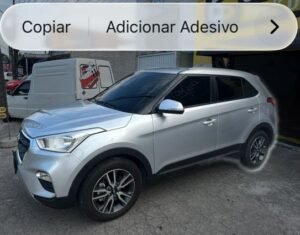 Fotografia de um Hyundai Creta 2018 prata estacionado em frente a uma garagem, com menu suspenso do iOS exibindo as opções "Copiar" e "Adicionar Adesivo".
