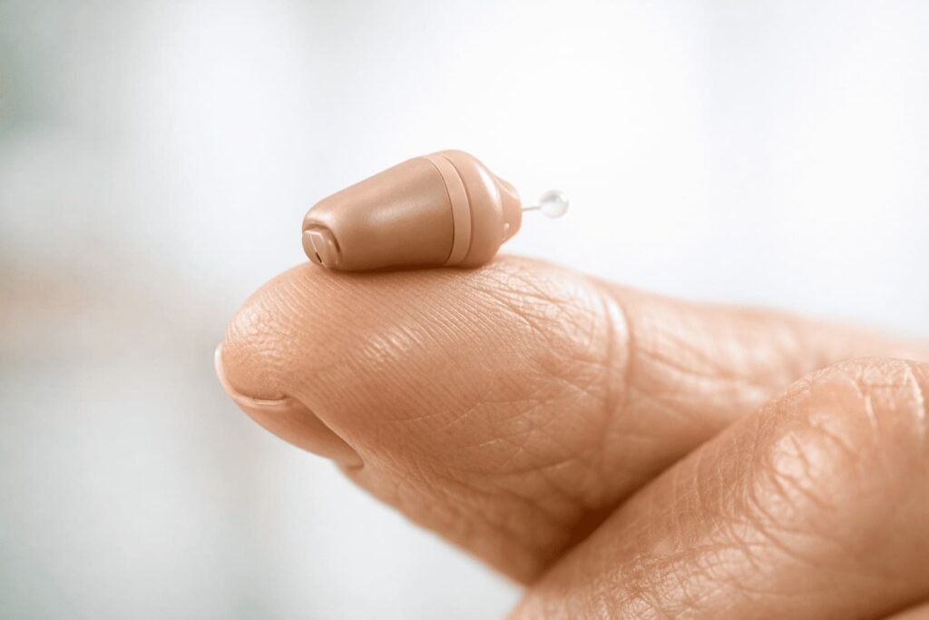 Pequeno aparelho auditivo invisível na ponta do dedo, mostrando a nova tecnologia discreta para tratamento de perda auditiva.